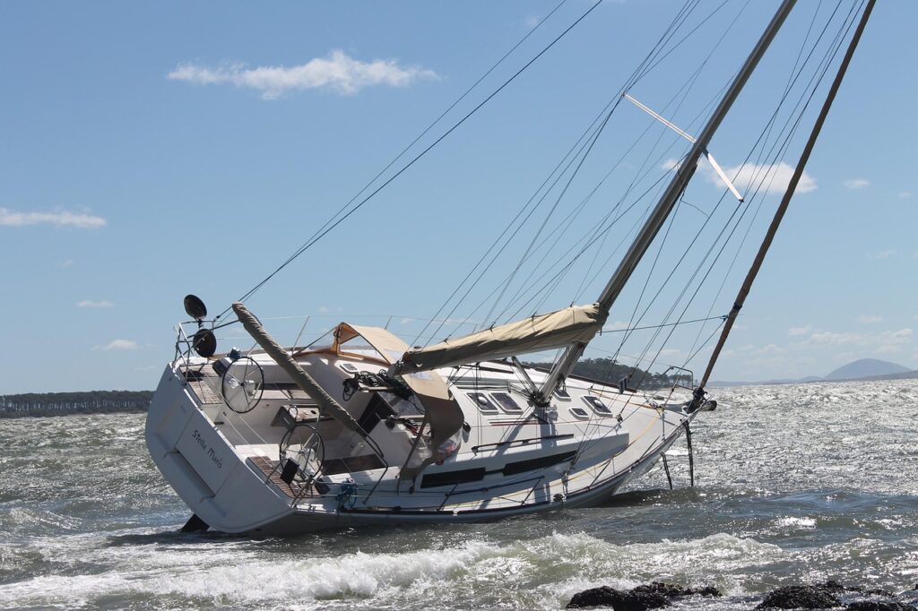 Barco de vela tumbado por un temporal cerca de la costa, ejemplo de los efectos de fenómenos climáticos extremos en el sector náutico