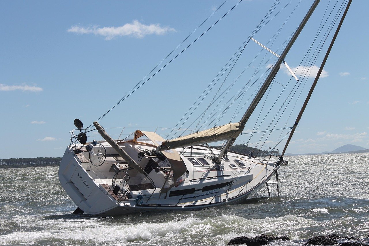Barco de vela tumbado por un temporal cerca de la costa, ejemplo de los efectos de fenómenos climáticos extremos en el sector náutico