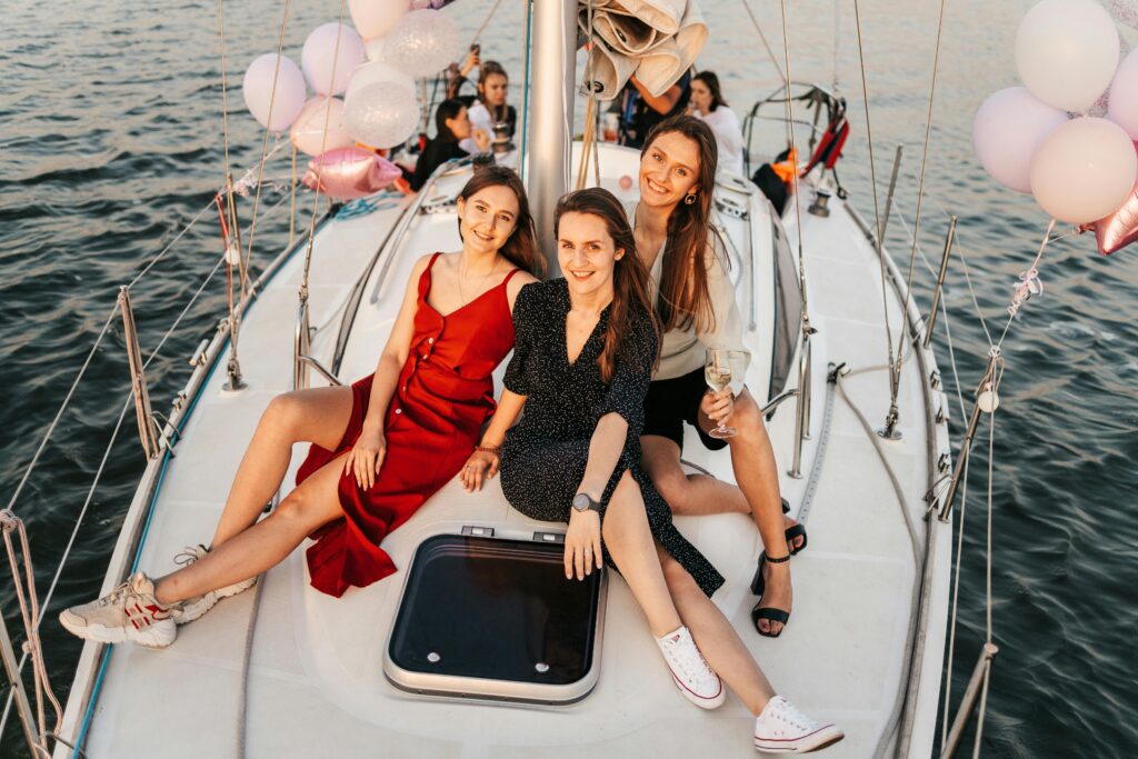 Grupo de mujeres disfrutando en la proa de un velero con copas y decoración festiva durante un charter de lujo.