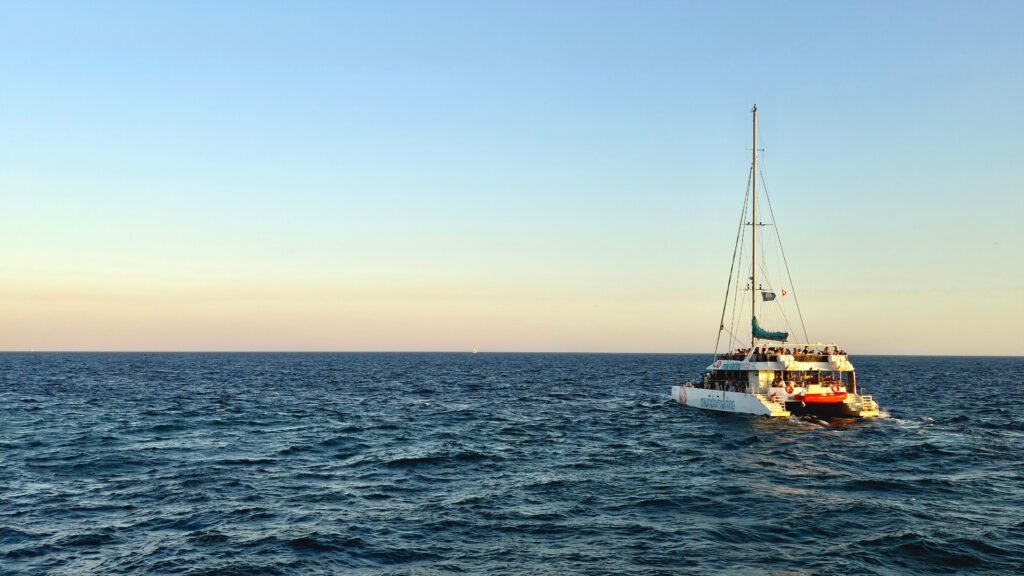 Catamarán con pasajeros navegando mar adentro al atardecer
